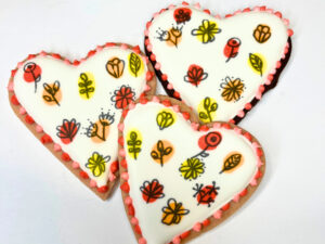 Three heart cookies decorated with royal icing and little flower design.