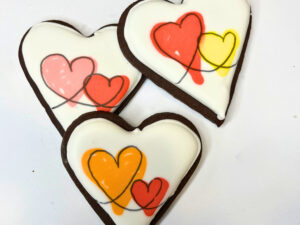 Three chocolate cookies with royal icing with two colourful hearts.