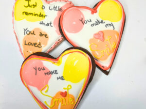Three heart cookies decorated with colour splotches and love messages.