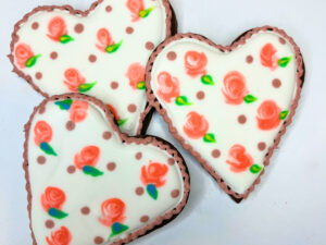 Three heart sugar cookies decorated with royal icing in a rose pattern.