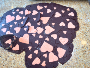 Two tone cookie dough that is chocolate with pink hearts. There is a metal heart cookie cutter on top of the dough.