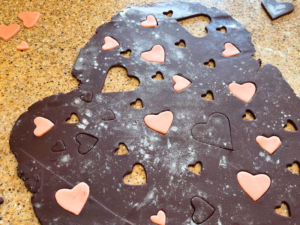 Chocolate cookie dough with different size hearts cut out. Pink cookie dough hearts are being placed in the spaces in the chocolate dough.