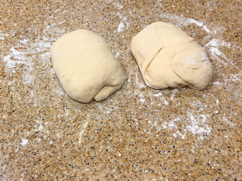 Two pieces of bread dough on a floured counter top.