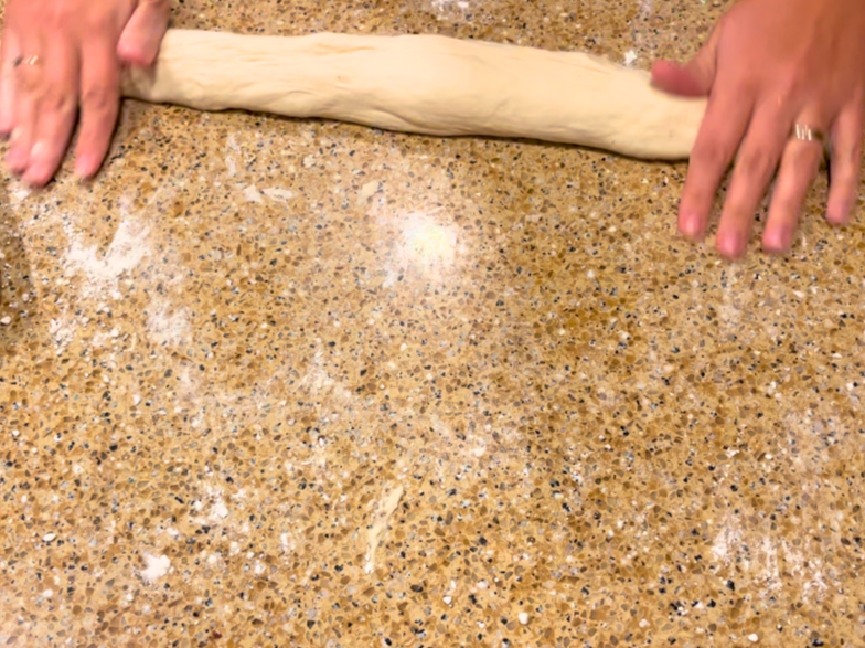 Woman rolling bread dough into a long log shape.