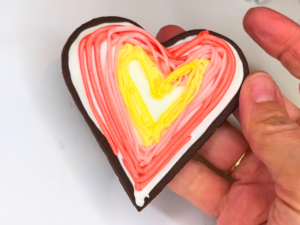 Woman holding a chocolate heart sugar cookie with colourful hearts drawn on the front in icing.