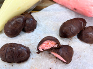 Some chocolate eggs on a piece of parchment paper. One is cut in half showing a pink filling.