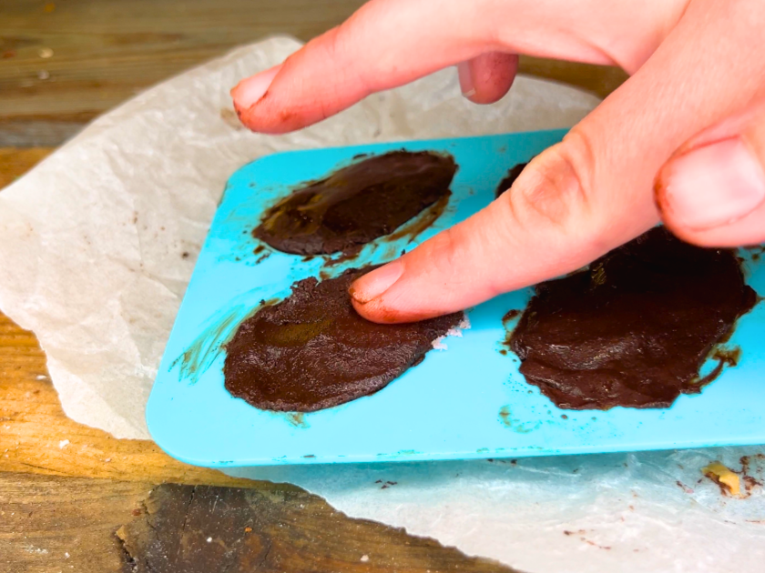 A woman pressing chocolate into a blue egg silicone mold.