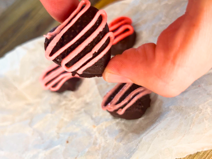 A woman holding a chocolate heart with a pink icing drizzle on top.