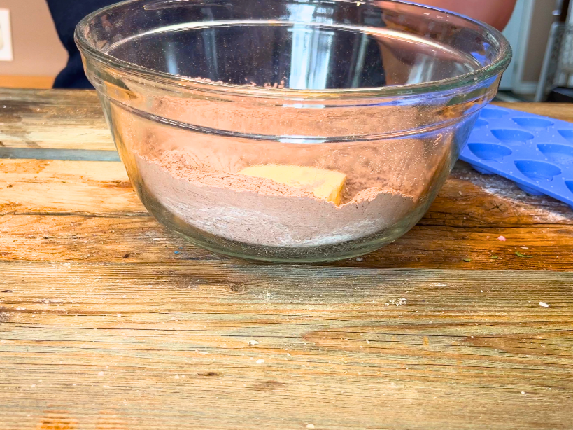 A glass bowl with icing sugar, cocoa, and butter inside.