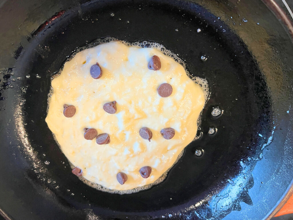 Pancake batter in a frying pan with chocolate chips on top.
