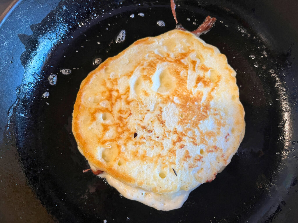 A pancake cooking on a frying pan.