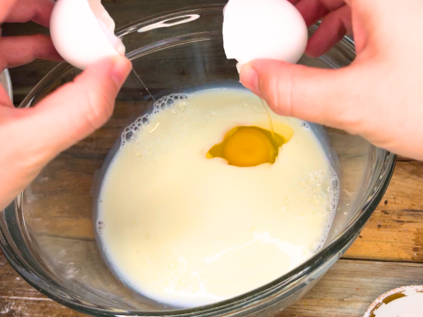 Woman breaking an egg into a bowl of milk.
