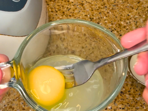 Woman holding a fork and a small measuring cup with lemon juice and egg in it.