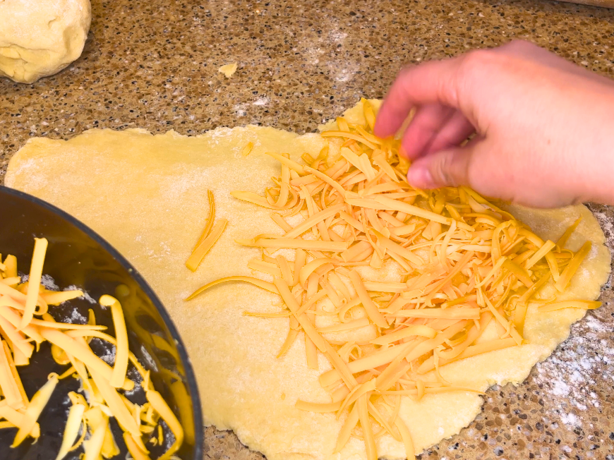 Woman spreading shredded cheese on a piece of dough.