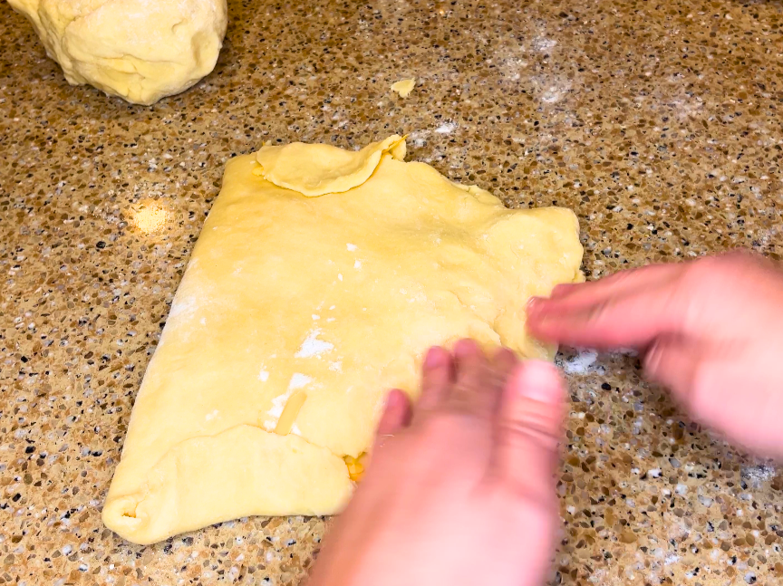Woman folding dough over to enclose in some shredded cheese.