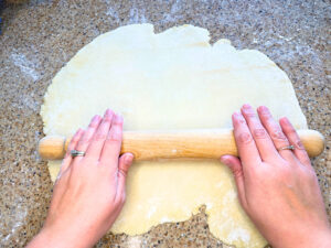 Woman rolling out dough with a wooden rolling pin.