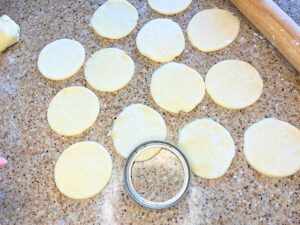 Dough cut into circles. There is a mason jar ring on the table as well.