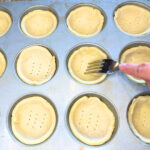 Woman using a fork to poke holes in pastry inside of muffin tins.