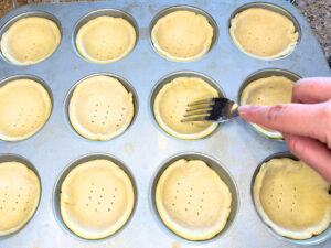 Woman using a fork to poke holes in pastry inside of muffin tins.