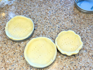 Three tart shells in Mason jar lids. The dough is not cooked.