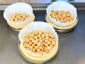Three tart shells in mason jar lids. There is a muffin liner in each with dried chickpeas.