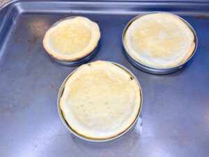 Three tart shells in canning jar lids on a baking sheet