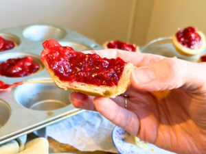 A woman holding a raspberry tart that is split in half. There are more tarts in the background.
