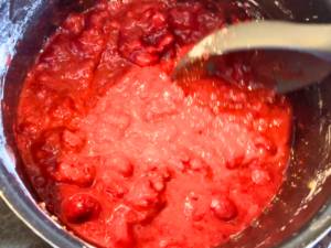 Raspberry pie filling being stirred inside of a sauce pot.