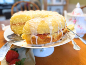 A circular vanilla cake with a red fruit filling and a white icing glaze on top. The cake is sitting on a cake pedestal.