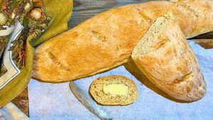 A French baguette on a table. One is sliced. The slice is in front with butter on it.