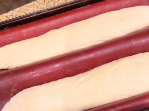 Two long dough baguettes that are separated by red silicone mats.