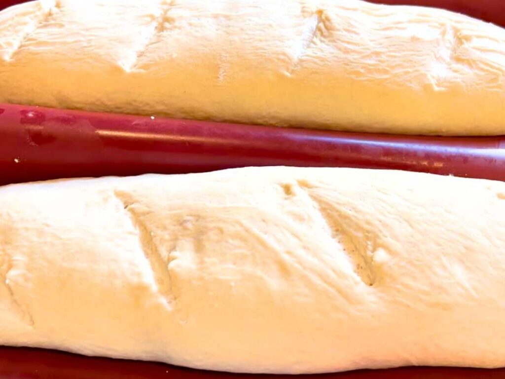 Two dough loaves of French bread with slashes cut on the tops.