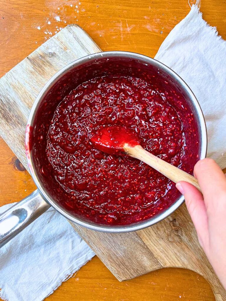 A woman is stirring a sauce pot filled with raspberry tart filling.