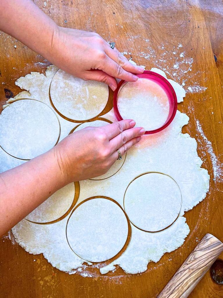 A woman is using a red circular cookie cutter to cut pie dough.