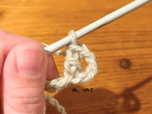 Woman holding grey yarn that has been formed into a double crochet. She is holding the yarn and the crochet hook.