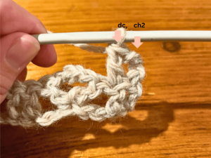 Woman holding grey yarn that she is using to crochet with a crochet hook.