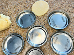 Mason jar lids on a counter top. There is a disc of dough in the background.