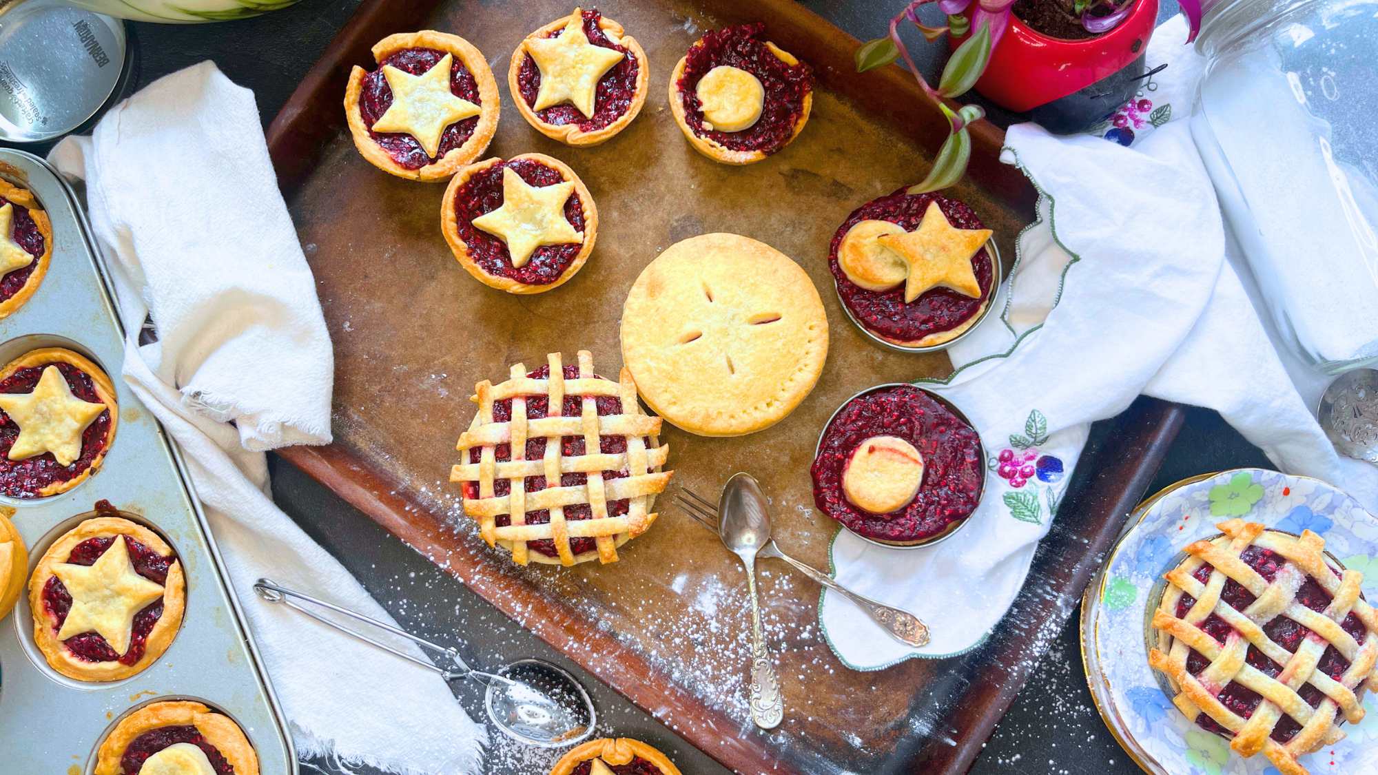 A stone baking sheet with mini raspberry tarts with double pie crusts like full, lattice, and star shape cut-outs.