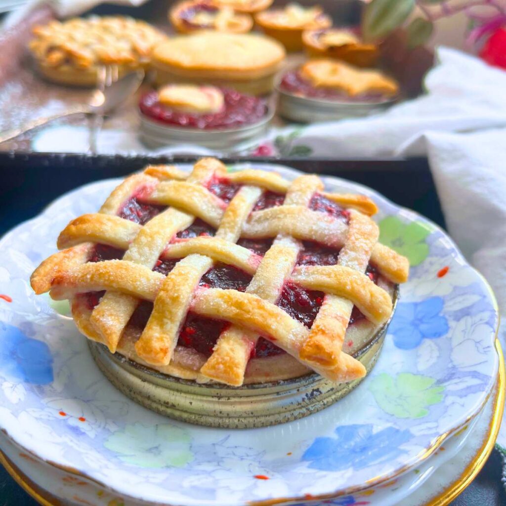 A lattice top raspberry tart in a Mason jar lid. there are more in the background.