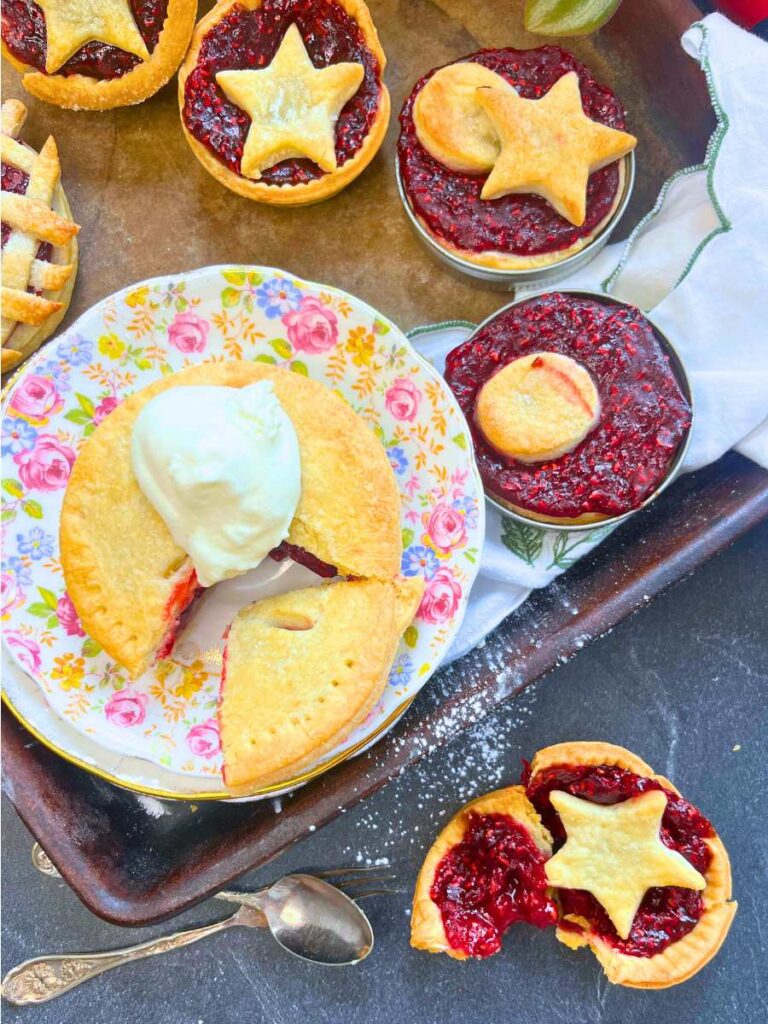 An assortment of mini raspberry tarts. In front one is broken in half.