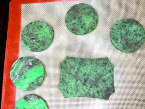 A lined baking sheet with green and black dough cutouts on it.