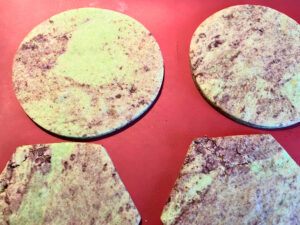 Four cutout cookie dough on a red baking mat. The dough is a green and black marbled appearance.