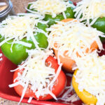 A casserole dish full of stuffed peppers with grated cheese on top.