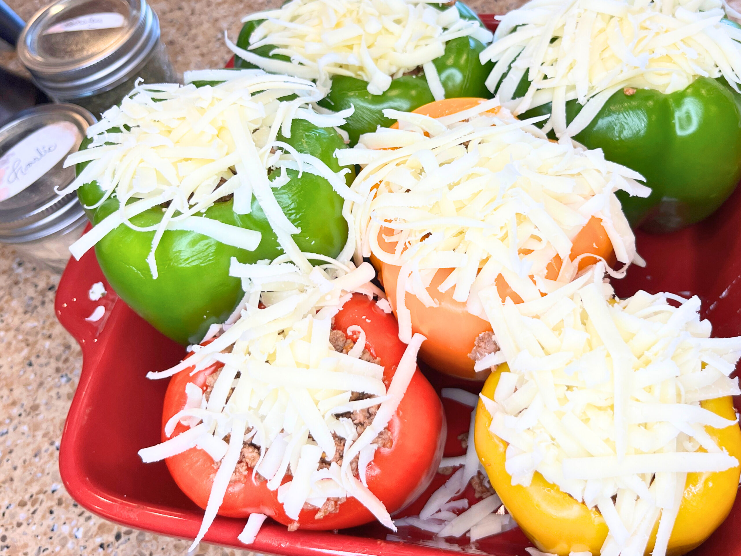 A casserole dish full of stuffed peppers with grated cheese on top.