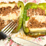 A plate with a stuffed pepper cut in half. There is ground meat and cheese inside.