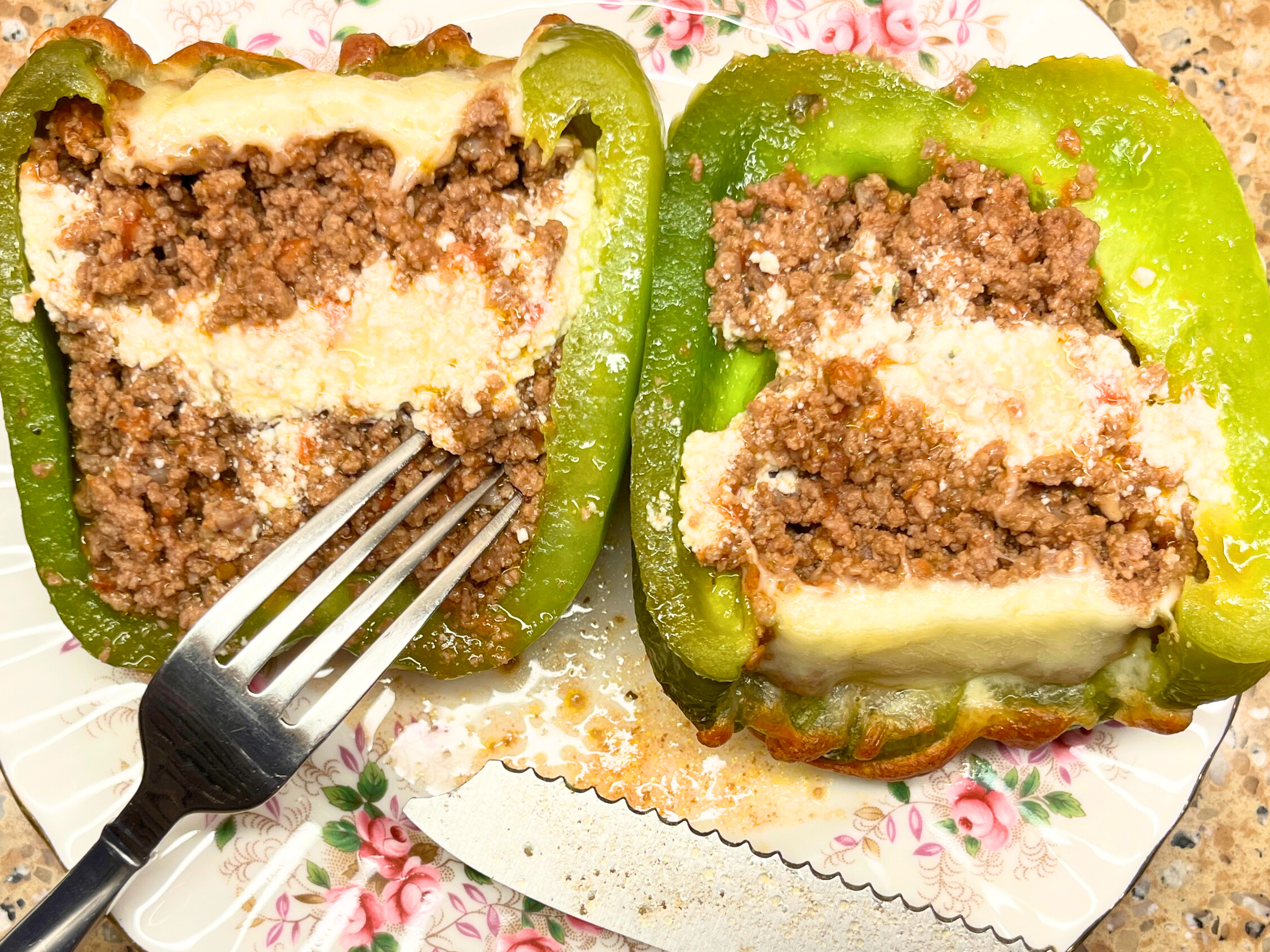 A plate with a stuffed pepper cut in half. There is ground meat and cheese inside.