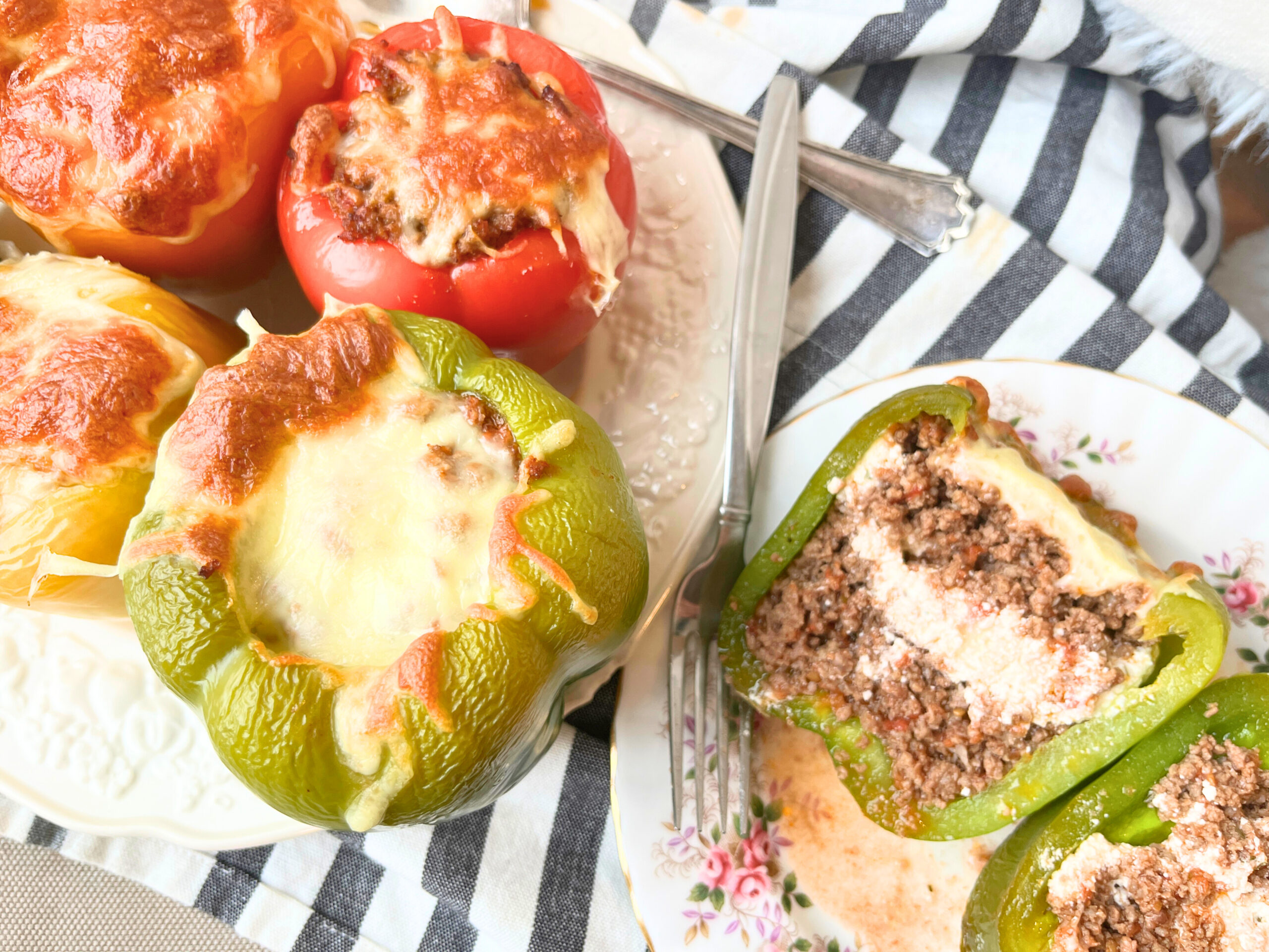 A plate of stuffed peppers there is a separate plate with one stuffed pepper cut in half. It is full of ground beef and cheese.