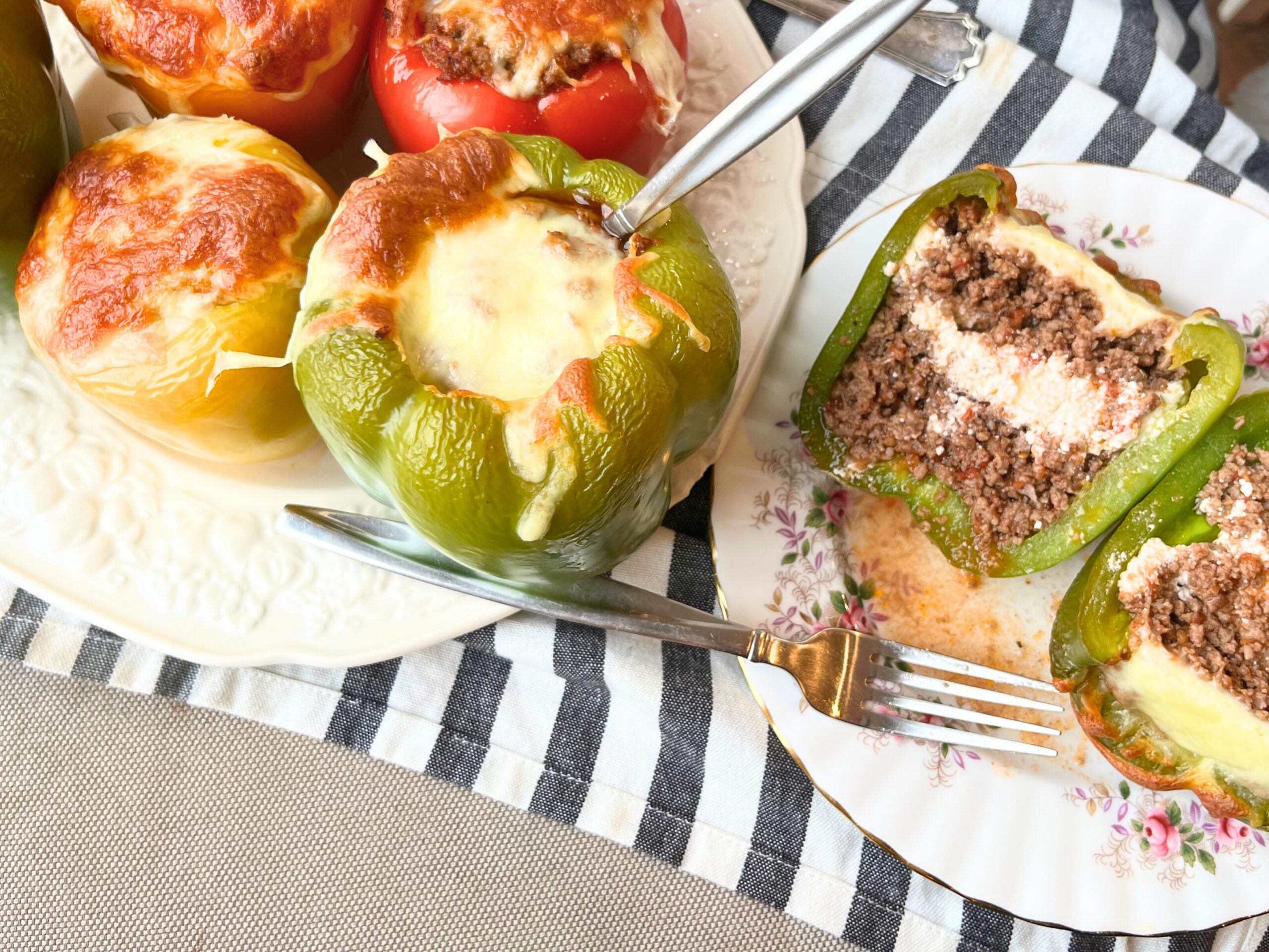 Some cooked stuffed peppers on a plate. There is one on a separate plate cut in half. They are full of meat and cheese.