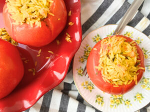 Some stuffed tomatoes with rice in a red dish. There is one on a yellow floral plate with a fork on it.
