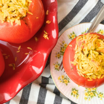 Some stuffed tomatoes with rice in a red dish. There is one on a yellow floral plate with a fork on it.